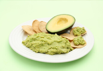 Delicious guacamole, avocado and chips on light green background