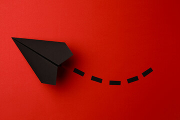 Handmade black paper plane with dotted lines on red background, top view