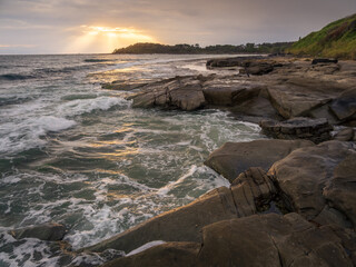 Fototapeta na wymiar Coastal Sunrise with Waves Crashing on Rocks