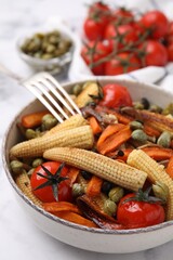 Tasty roasted baby corn with tomatoes and capers on white marble table, closeup