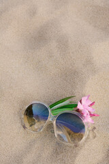 Fototapeta na wymiar Beautiful sunglasses with tropical flower on sandy beach, space for text