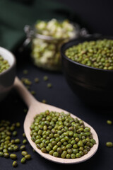 Different dishware with green mung beans on black background, closeup