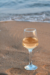 Glass of tasty wine on sand near sea, space for text