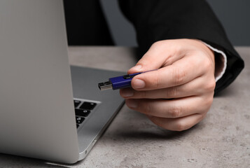 Man with usb flash drive near laptop at grey table, closeup