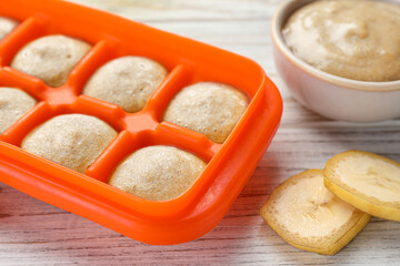 Banana puree in ice cube tray with ingredients on white wooden table, closeup