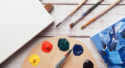 Artist's palette with samples of colorful paints, brushes and canvases on white wooden table, flat...