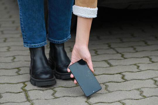 Woman taking dropped smartphone from pavement, closeup. Device repairing