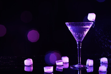 Glass of martini with ice in neon lights on dark background, bokeh effect. Space for text