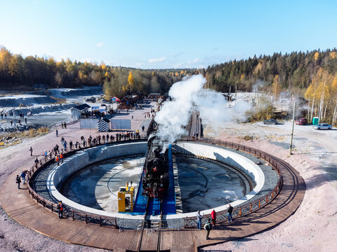 The train is surrounded by an autumn forest, lake, canyon, and quarry from above. The Ruskeala Park view from the drone