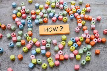 The word HOW? written on the post-it note surrounded by colorful beads
