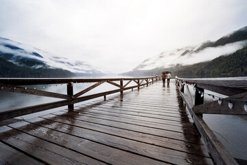 
A young sympathetic couple stands with an umbrella in their hands against the backdrop of a beautiful lake and mountains.