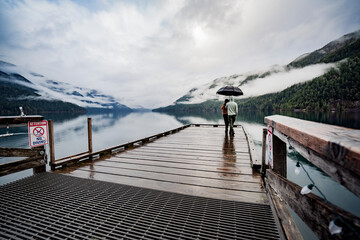 
A young sympathetic couple stands with an umbrella in their hands against the backdrop of a beautiful lake and mountains.