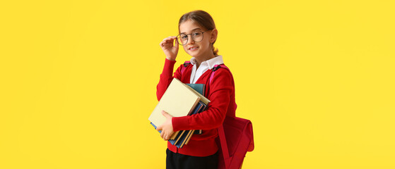 Cute little school girl with books on yellow background