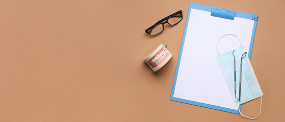 Clipboard, medical mask, dental tools, jaw model and eyeglasses on brown background with space for text