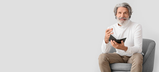 Senior male psychologist sitting in armchair on light background with space for text