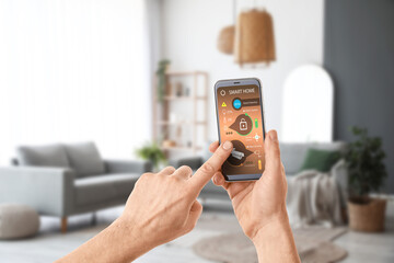 Man's hands holding mobile phone with smart home security system on screen in living room