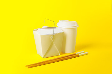 Paper box with Asian food, cup and chopsticks on color background