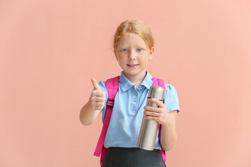 Little redhead schoolgirl with thermos showing thumb-up on color background