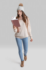 Young woman in warm hat reading book on grey background