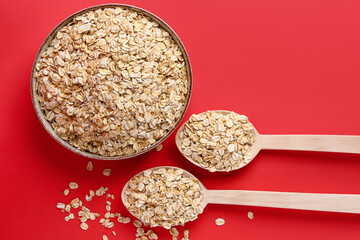 Bowl and spoons of raw oatmeal on red background