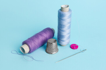 Thread spools, needle, button and thimble on color background