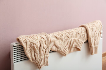 Warm sweater drying on electric radiator near pink wall, closeup