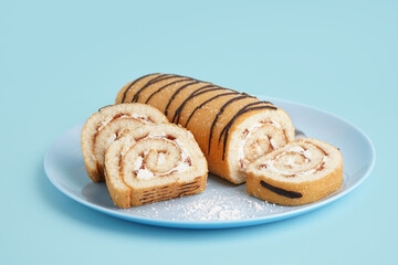 Plate with delicious sponge cake roll on color background