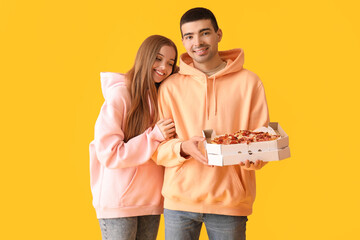 Happy young couple with fresh pizza on yellow background