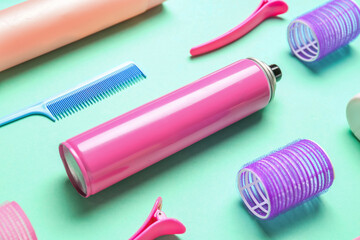 Hair spray with curlers, comb and clips on green background, closeup