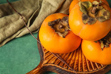 Wooden board with ripe persimmons on color table, closeup
