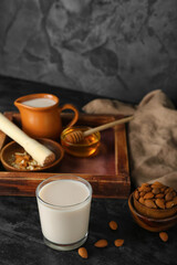 Glass of healthy almond milk and nuts on dark background