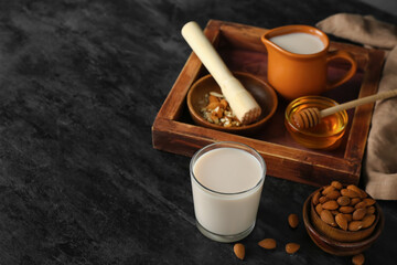 Glass of healthy almond milk and nuts on dark background