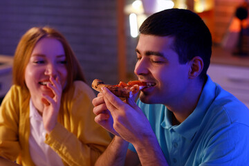 Young couple eating tasty pizza in kitchen at night, closeup