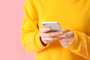 Young woman using mobile phone on pink background, closeup