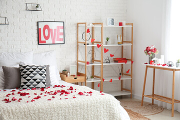 Interior of light bedroom decorated for Valentine's Day with rose petals, shelving unit and tables