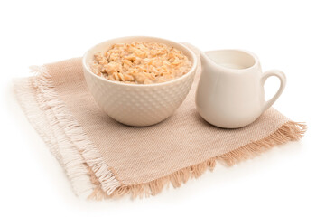 Bowl of tasty oatmeal, pitcher with milk and napkin isolated on white background