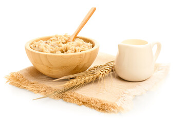 Wooden bowl of tasty oatmeal, pitcher with milk, wheat ears and napkin isolated on white background