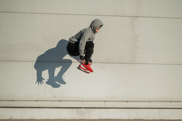Caucasian man in hoodie jumping high with hands on knees outdoors. 