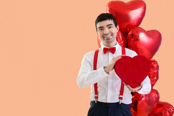 Young man with gift and balloons on beige background. Valentine's Day celebration