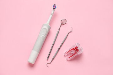 Plastic tooth with dental tools and electric brush on pink background