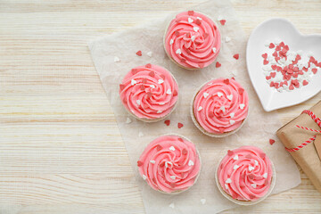 Baking paper with cupcakes, plate and sprinkles for Valentine's Day on wooden background
