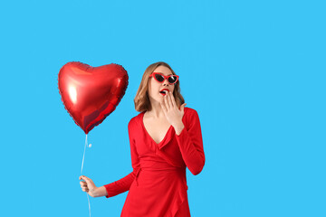 Beautiful surprised young woman with red heart-shaped balloon on blue background