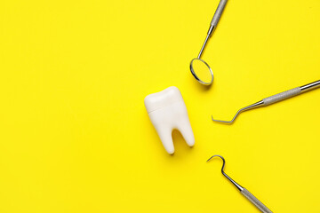 Plastic tooth with dental tools on yellow background