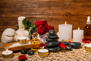 Fototapeta na wymiar Spa stones with burning candles and roses on wooden table, closeup. Valentine's Day celebration
