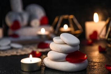 Spa stones with rose petal and candle on dark table, closeup. Valentine's Day celebration