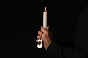 Hands of Jewish man with candle and dog tag honoring victims of Holocaust on dark background