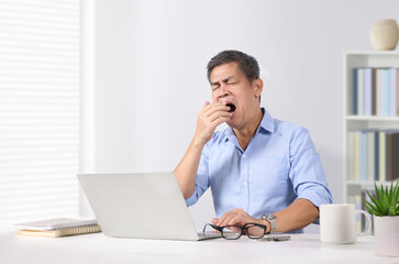 Businessman yawning in front of the laptop at office desk.