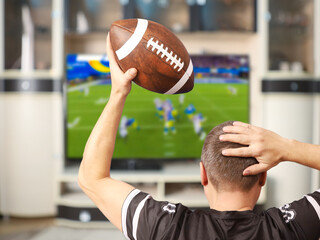 Fan of american football. Man with a ball watching TV.
