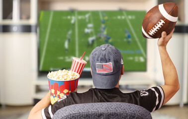 Fototapeta Fan of american football. Man with a ball watching TV. obraz