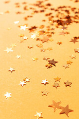 Shiny stars confetti scattered on a gold colored background. Selective focus.